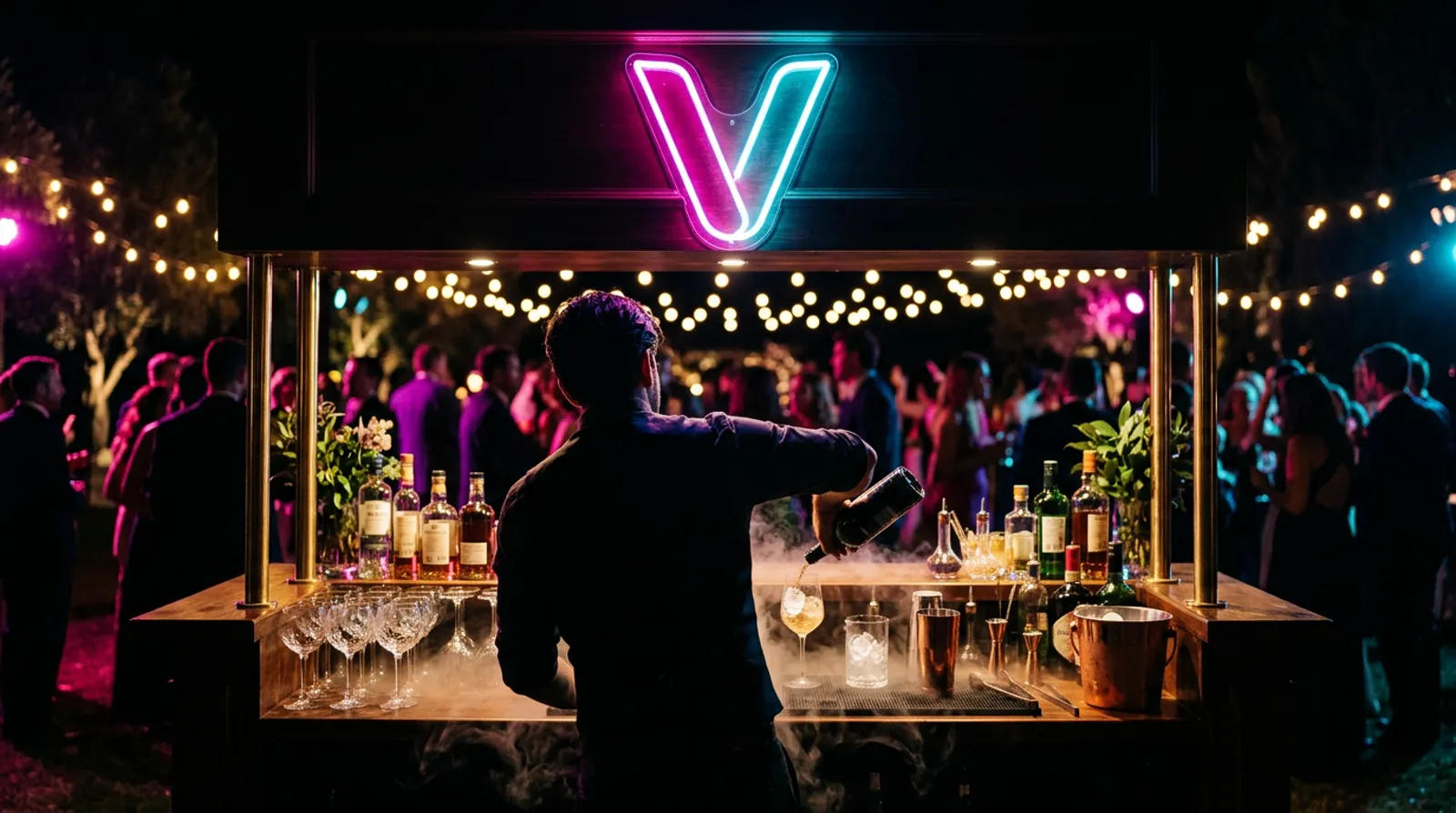 Bartender za mobilnim barom sa neonskim slovom V, gosti u bašti pod svetlima